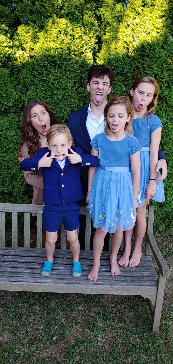 Five siblings making playful faces on a garden bench